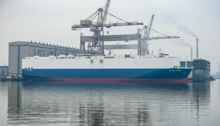 Огромный новый автовоз MV Ocean Explorer у причала судостроительного завода на фоне портовых кранов в Китае.